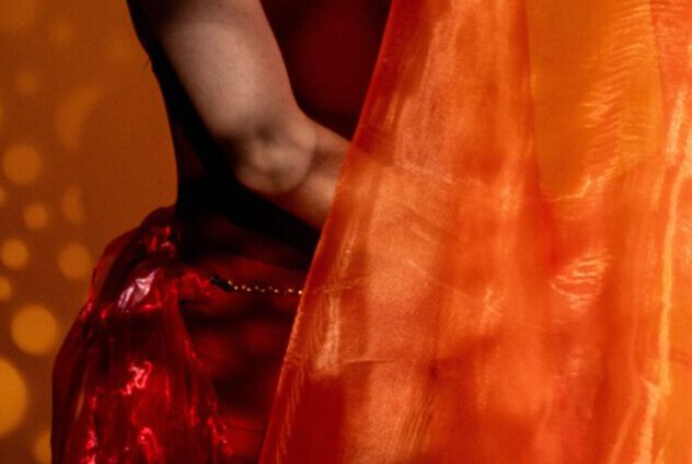 Graceful woman in an orange dress dances with fabric in artistic lighting.